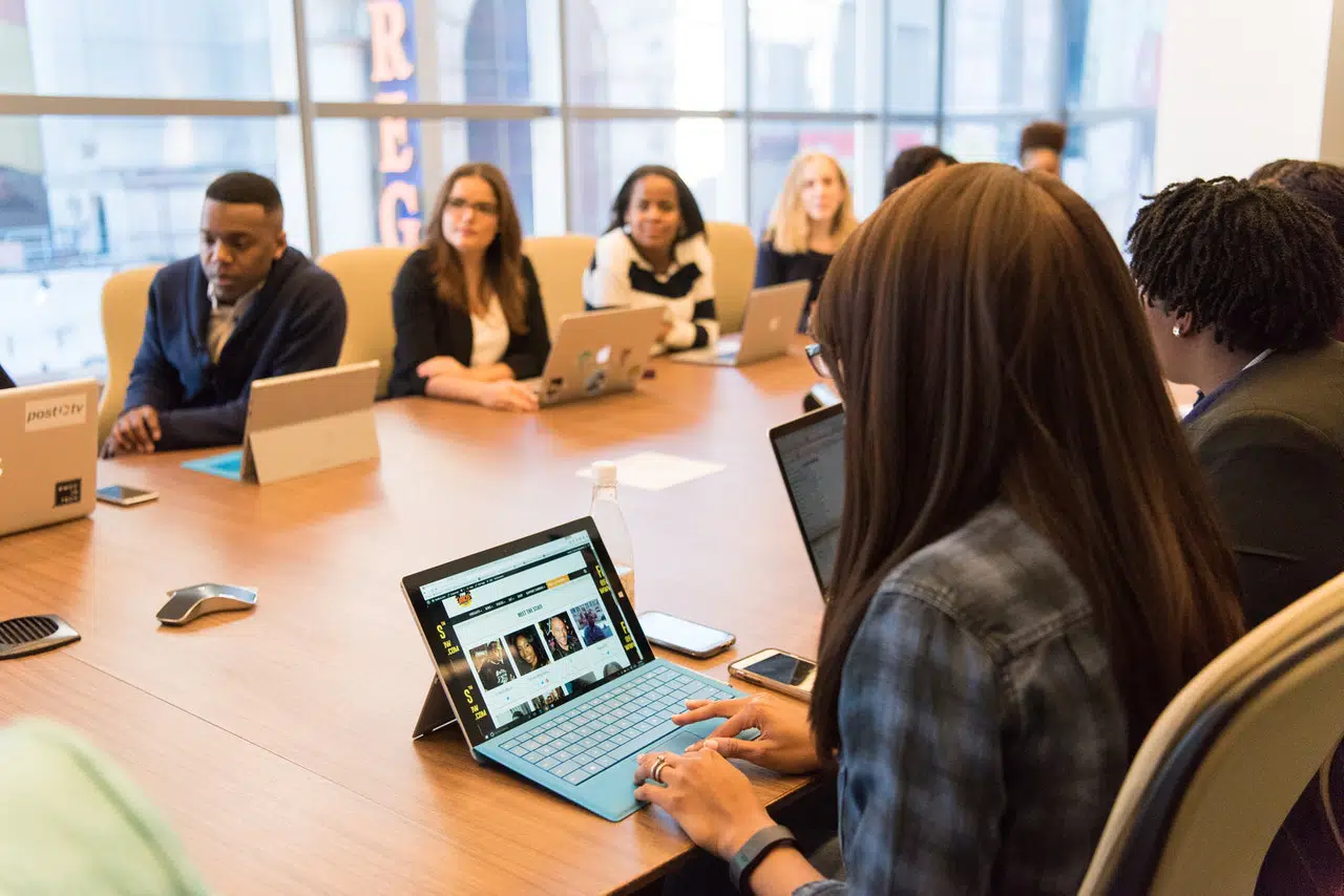 Photo of Meeting at a conference table with multiple attendees consulting a laptop